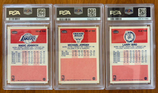 Backs of three graded 1986 Fleer basketball cards displayed side by side: Magic Johnson #53 PSA 7, Michael Jordan rookie card #57 PSA 5.5, and Larry Bird #9 PSA 8. The card backs show player biographies, career statistics, and team logos for the Los Angeles Lakers, Chicago Bulls, and Boston Celtics.