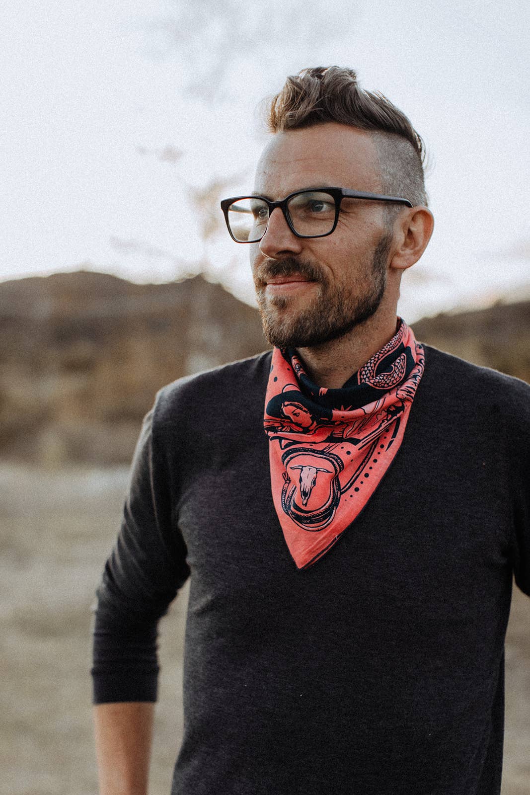 Model wearing the Bandits Rattle & Hiss bandana by Nuri Amanatullah tied as a neckerchief with a black sweater, showcasing the longhorn skull and Southwestern-inspired artwork.