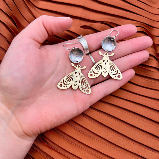 gold silver moth earrings, mixed metal moth jewelry, gold over silver earrings, celestial moth earrings, forest-inspired jewelry, brass and silver moth earrings, artisan moth earrings, hypoallergenic gold filled earrings, sterling silver moth jewelry, moonlight inspired earrings, fantasy woodland earrings, handcrafted insect earrings, dnd forest fae jewelry, nature inspired statement earrings, moth earrings for sensitive ears