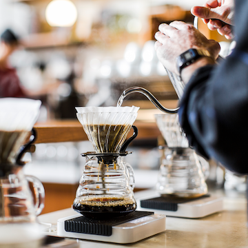 Barista brewing Sightglass Coffee with a pour-over dripper in a bright café.