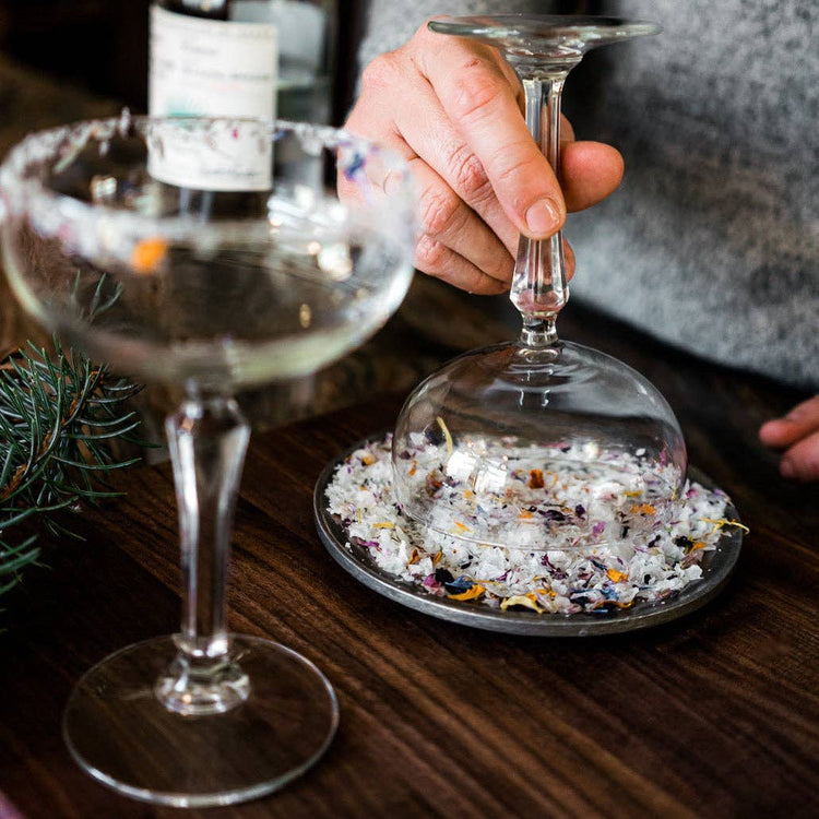 Cocktail glass being rimmed with FLOUWER CO. floral garnishing salt and edible flower petals.