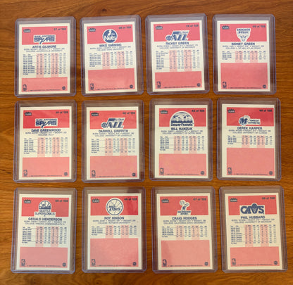 Backs of 1986 Fleer Basketball cards #37–48 from the complete 1986–87 Fleer Basketball set. Card backs feature player statistics, biographical information, and team logos for Artis Gilmore, Mike Gminski, Rickey Green, Sidney Green, Dave Greenwood, Darrell Griffith, Bill Hanzlik, Derek Harper, Gerald Henderson, Roy Hinson, Craig Hodges, and Phil Hubbard. Cards are arranged in numerical order and shown in protective holders on a wood tabletop.
