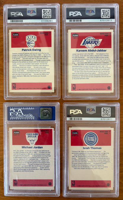 Backs of four graded 1986 Fleer Basketball stickers displayed on a wood surface. Featured stickers include Patrick Ewing #6 PSA 8, Kareem Abdul-Jabbar #1 PSA 6, Michael Jordan #8 PSA 7, and Isiah Thomas #10 PSA 5. The sticker backs contain player biographies and career highlights and are encapsulated in authenticated PSA holders.
