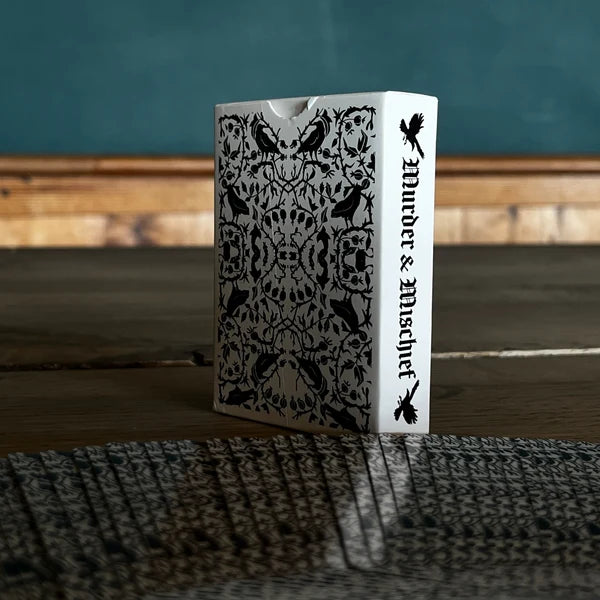 Black-and-white Murder & Mischief playing card tuck box standing on a dark tabletop