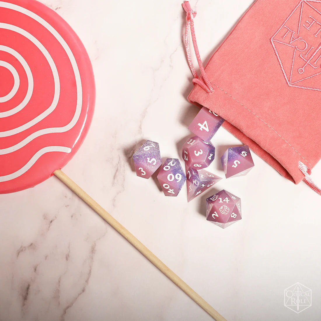 Set of purple polyhedral dice with a pink drawstring bag. The image on the 20 side of the d20 die is cupcake image, icon of Jester lavorre.