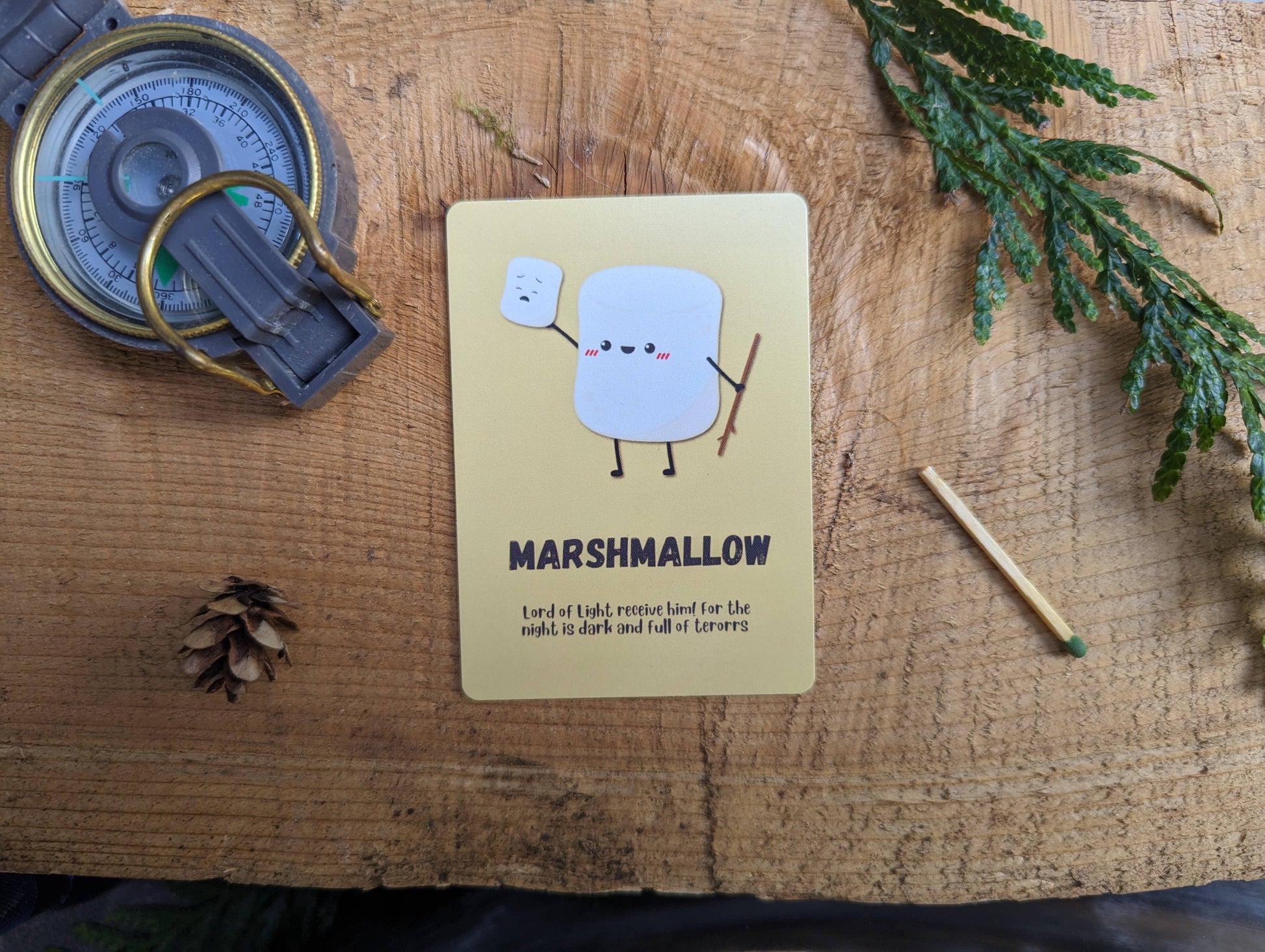 Marshmallow character card on a wooden surface with a compass and matchbook.