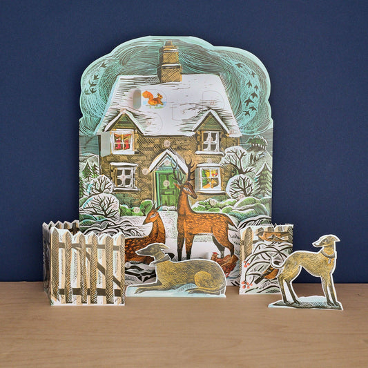 Angela Harding Christmas Cottage Advent Calendar featuring a snowy cottage with stand-up deer, birds, and 24 advent windows.