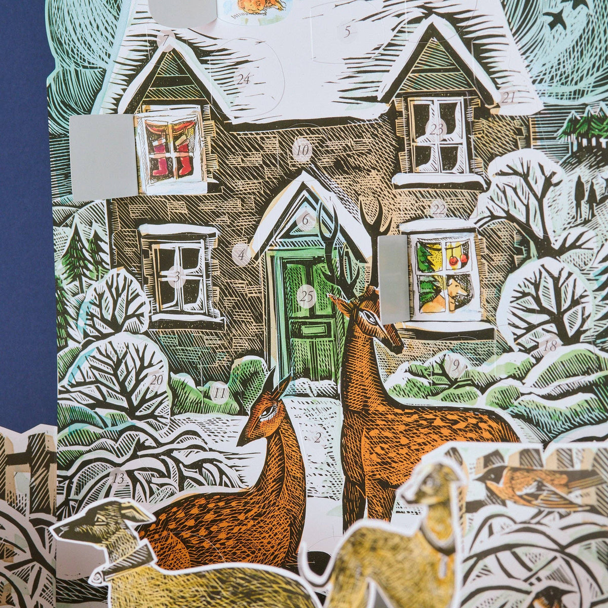 Close-up of the Angela Harding Christmas Cottage Advent Calendar showing opened advent windows with illustrated holiday scenes behind the doors.