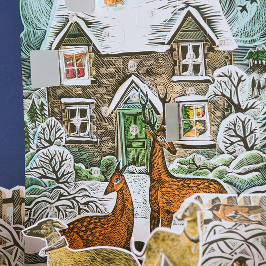 Close-up of the Angela Harding Christmas Cottage Advent Calendar showing opened advent windows with illustrated holiday scenes behind the doors.