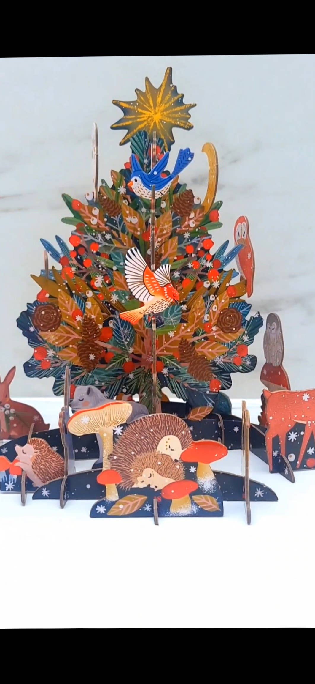 Vertical view of the Antoana Oreski Beneath the Tree Pop & Slot Advent Calendar fully assembled into a three-dimensional Christmas tree surrounded by woodland animals, birds, mushrooms, and festive forest details.
