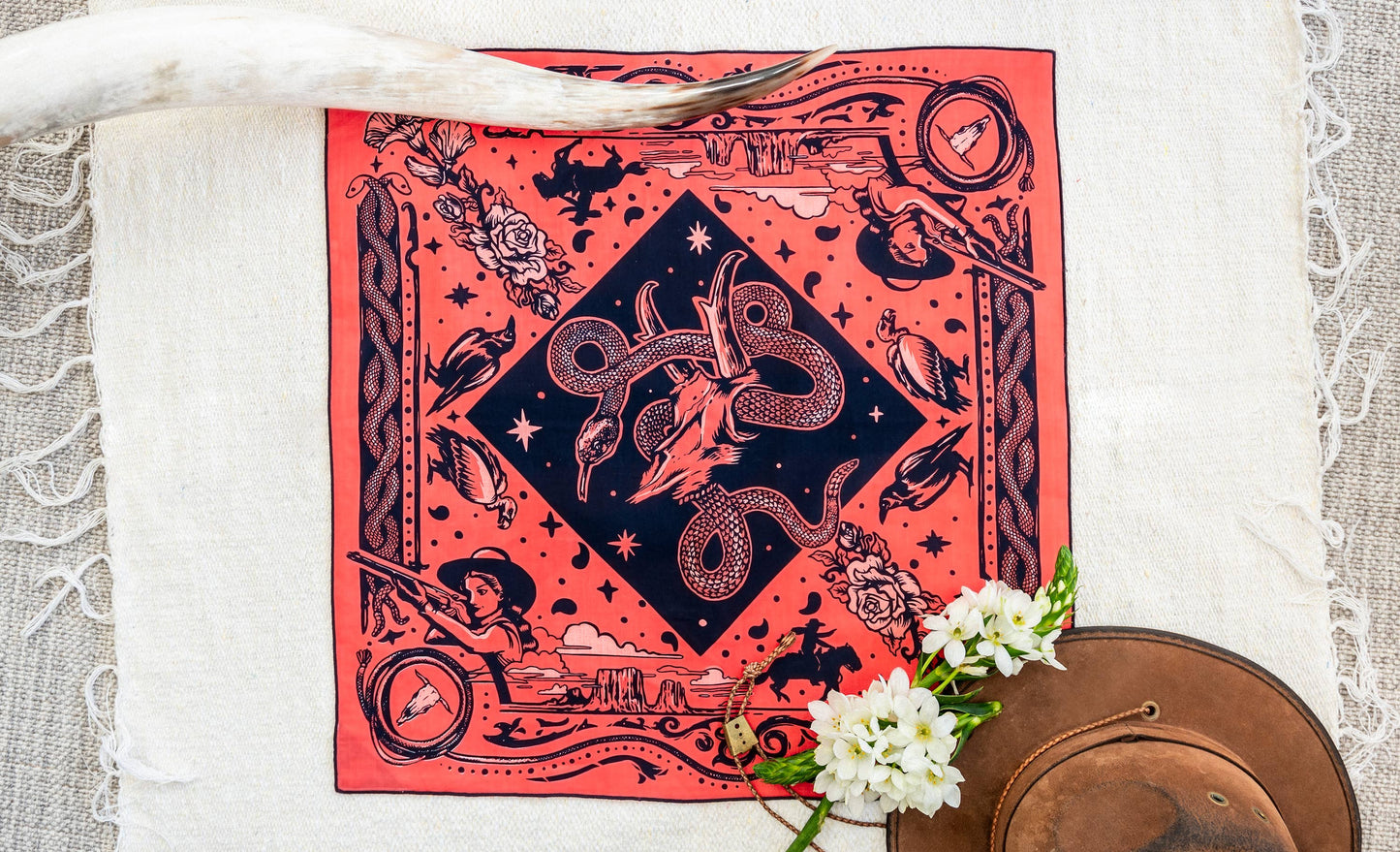 Bandits Rattle & Hiss bandana by Nuri Amanatullah featuring a coiled rattlesnake around a longhorn skull, surrounded by desert birds, wildflowers, stars, and Southwestern-inspired illustrations.