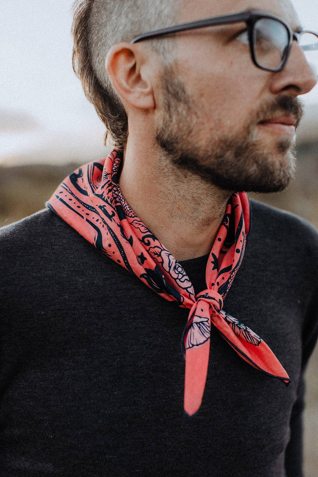 Model wearing the Bandits Rattle & Hiss bandana by Nuri Amanatullah tied as a rolled neck scarf with a black sweater.