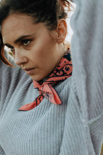 Model wearing the Bandits Rattle & Hiss bandana by Nuri Amanatullah tied close around the neck with a light gray knit sweater.