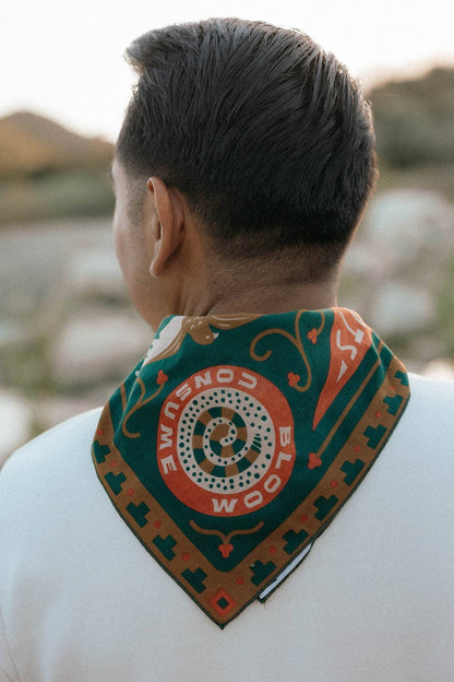 Rear view of a model wearing the Bandits Greenbelt bandana by Sam Larson around the neck, showing the "Bloom & Consume" emblem and nature-inspired artwork.