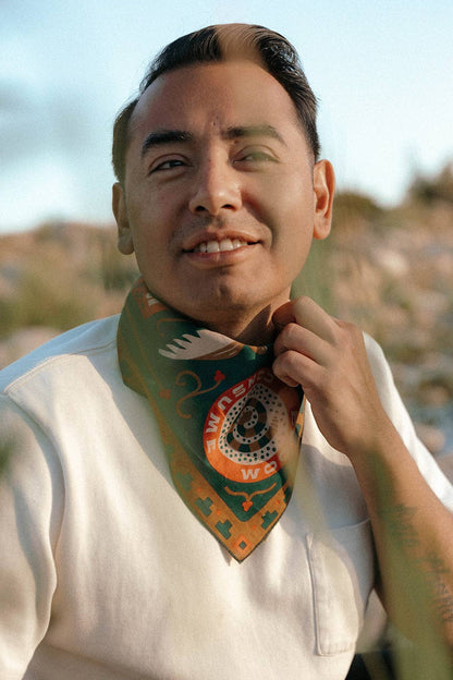 Model wearing the Bandits Greenbelt bandana by Sam Larson tied as a neck scarf with a white T-shirt, showcasing the nature-inspired artwork and "Bloom & Consume" emblem.