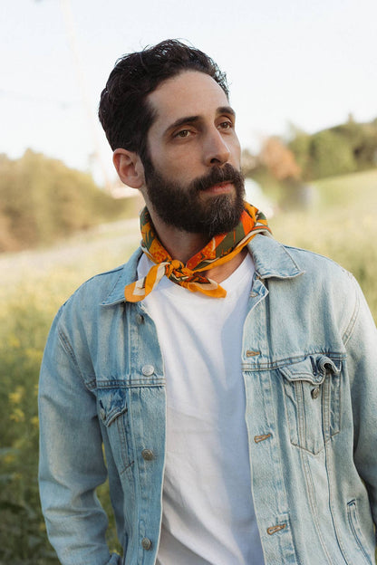 Model wearing the Bandits Sunset bandana by Studio MUTI tied as a compact neck tie with a denim jacket in a field of wildflowers.
