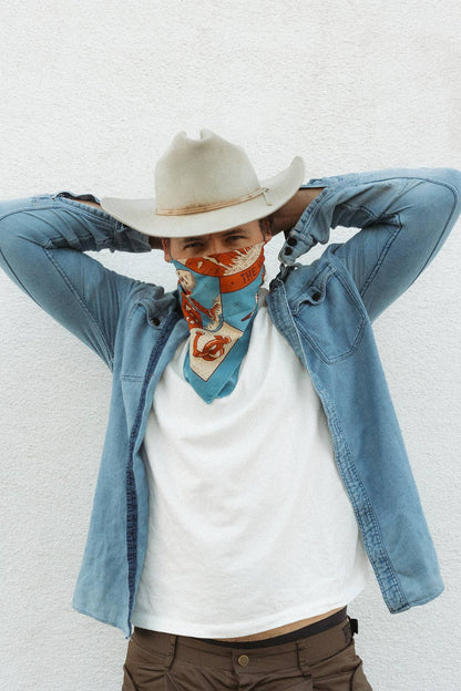Model wearing the Bandits Wild West bandana by Van Berkemeyer as a face covering with a cowboy hat, denim overshirt, and white T-shirt.