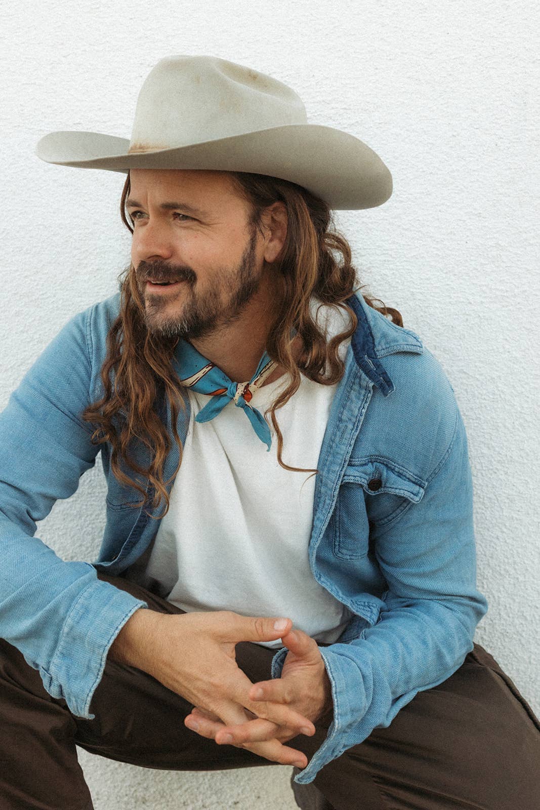 Model wearing the Bandits Wild West bandana by Van Berkemeyer tied as a neckerchief with a cowboy hat, denim overshirt, and white T-shirt.