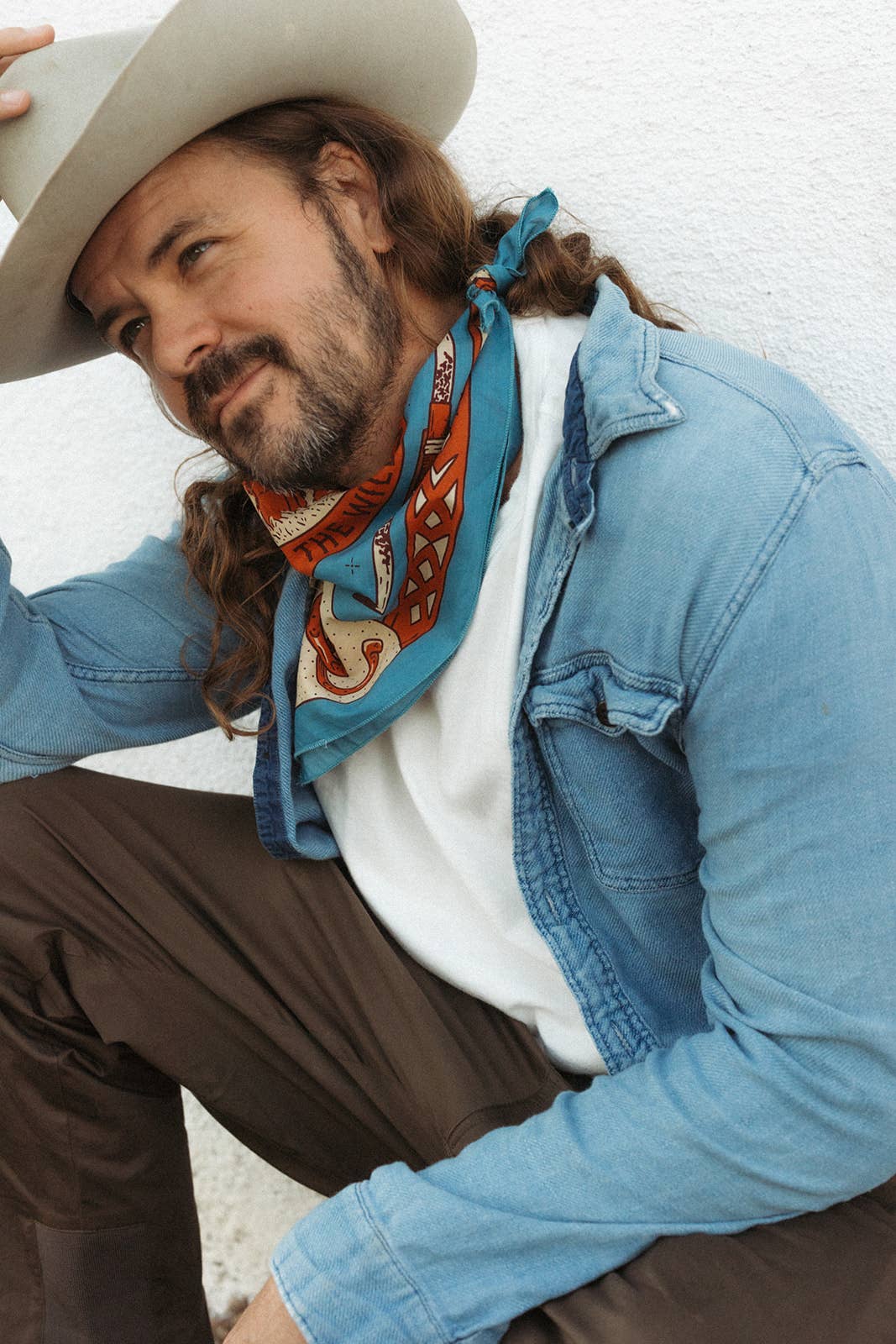 Model wearing the Bandits Wild West bandana by Van Berkemeyer tied as a neck scarf with a cowboy hat and denim overshirt.