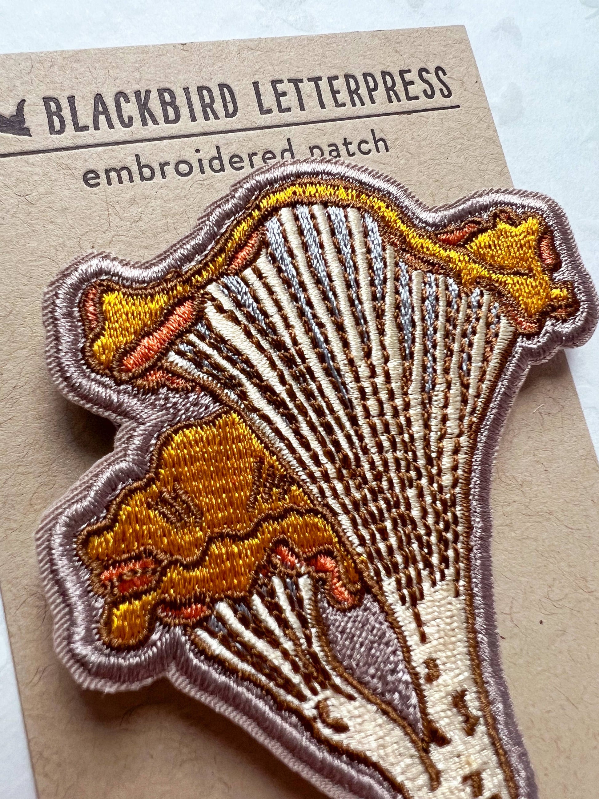chanterelle mushroom patch, embroidered mushroom patch, golden mushroom iron-on, fungi sew-on patch, woodland embroidery patch, textured chanterelle applique, backpack mushroom patch, jean jacket patch, forager gift, artisan embroidered patch, blackbird letterpress patch, cottagecore mushroom accessory, nature lover patch, rogue & rye mushroom patch, embroidered chanterelle design
