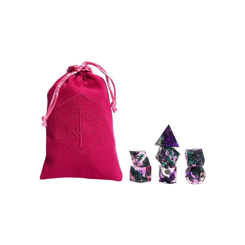 Dark pink Critical Role velveteen dice bag displayed beside the Critical Role Champion Dice Set inspired by Caduceus Clay. The seven sharp-edged resin dice feature swirling pink, purple, black, and green colors with iridescent shimmer and botanical-style inclusions, reflecting the character’s connection to nature and the Blooming Grove.