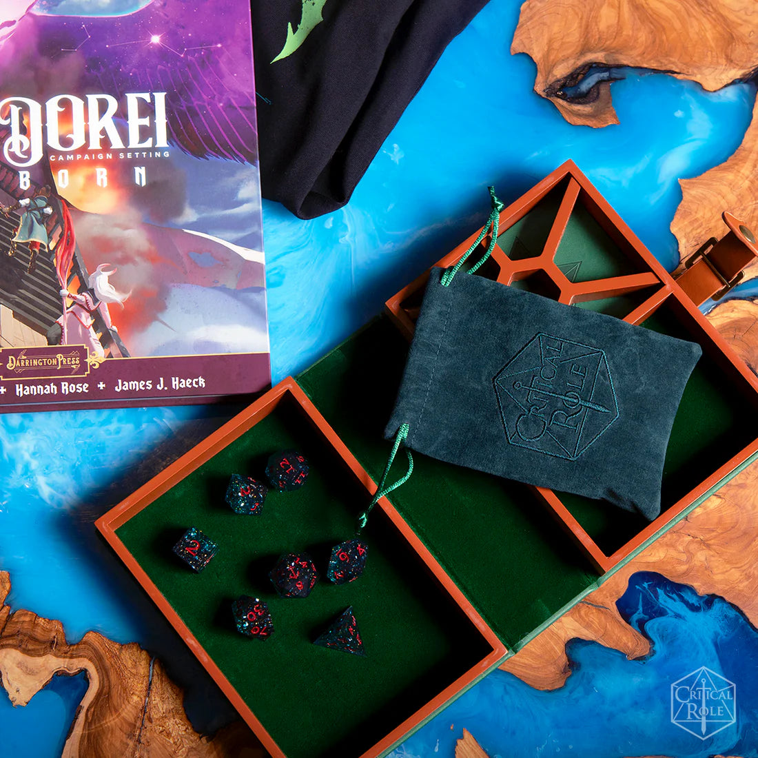 Game components including dark teal and red Fjord Stone dice, included teal embroidered critical role dice bag, and a book on a map-themed surface.