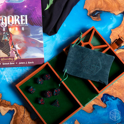 Game components including dark teal and red Fjord Stone dice, included teal embroidered critical role dice bag, and a book on a map-themed surface.