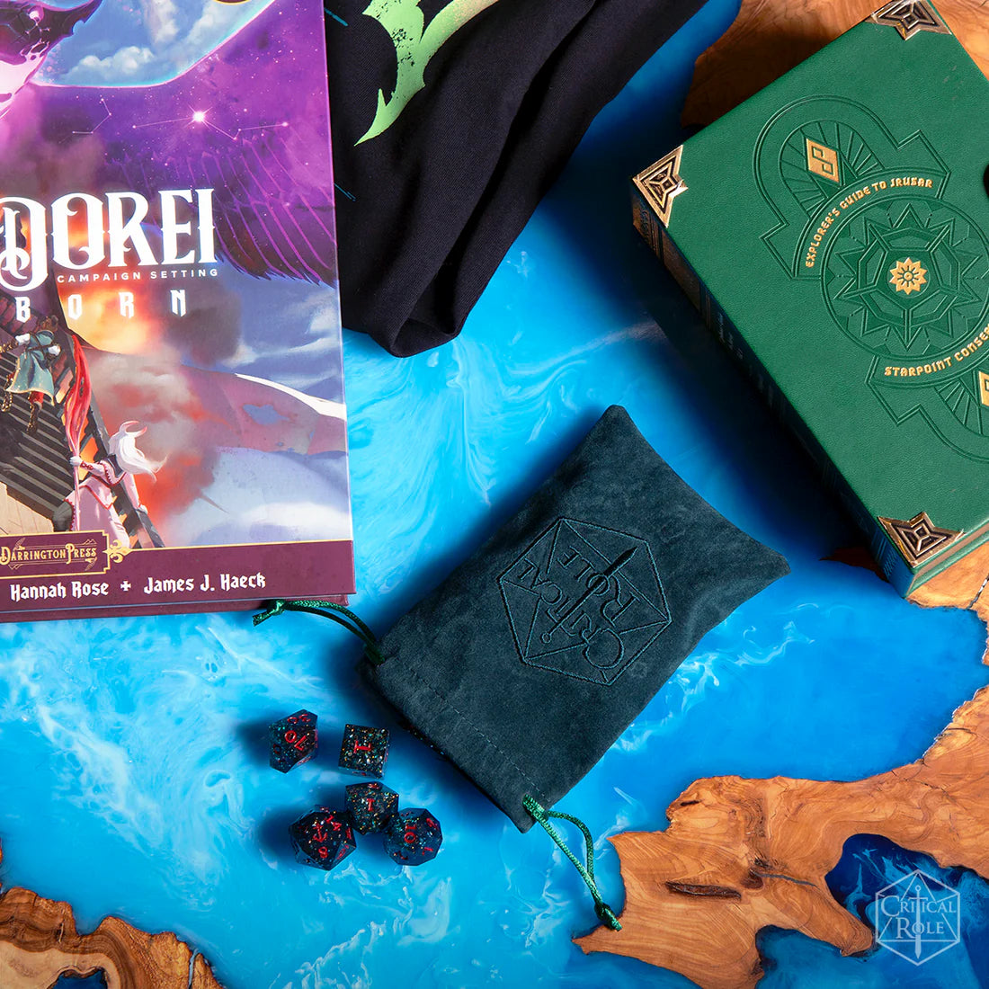 Collection of gaming items including a Tal'Dorei campaign book, Fjord Stone dice, and included dark teal embroidered pouch on a blue surface