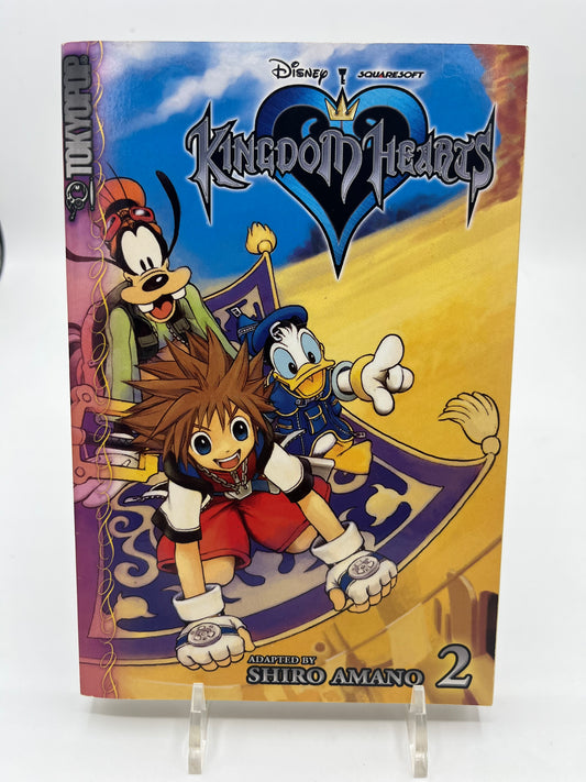 Cover of Kingdom Hearts Volume 2 manga by Shiro Amano featuring Sora, Donald Duck, and Goofy flying on a magic carpet beneath the Kingdom Hearts logo.