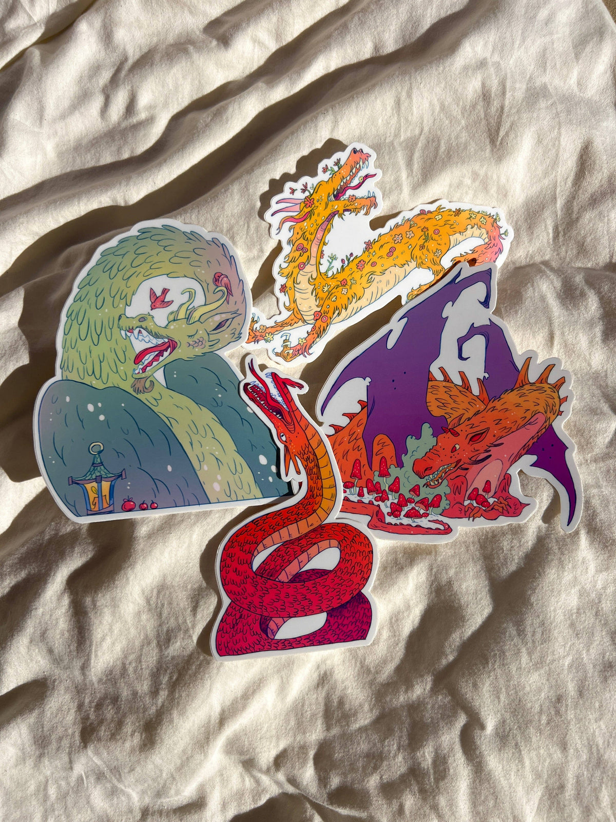 Four colorful Natalie Andrewson dragon stickers arranged on fabric