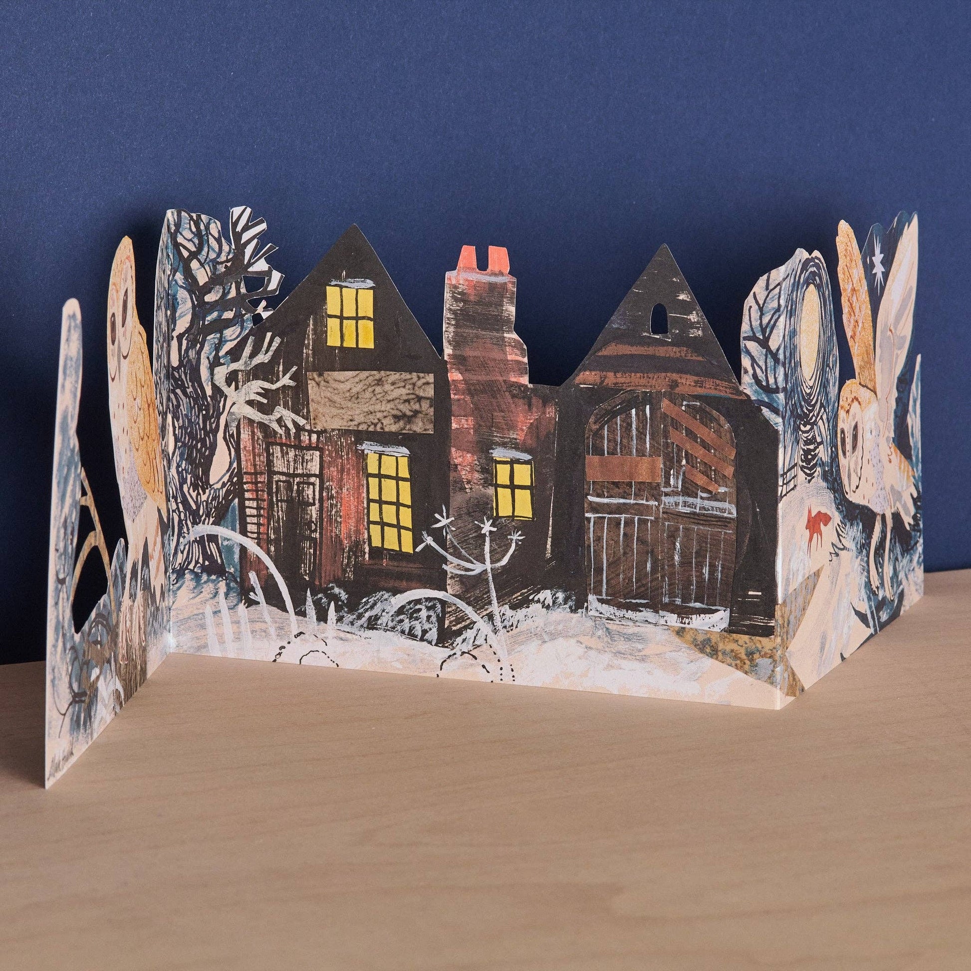 Close-up of the Mark Hearld Silent Flight accordion card showing woodland houses, snowy trees, and winter illustrations.