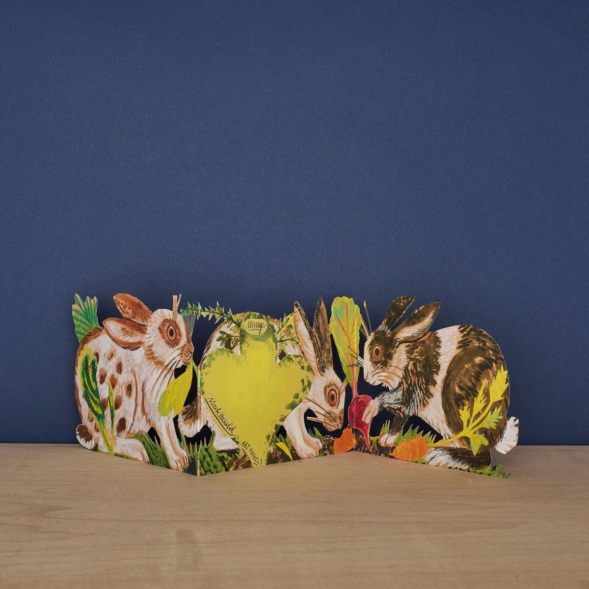 Mark Hearld Three Fold Rabbits accordion greeting card showing the hidden clover-shaped message panel surrounded by illustrated rabbits and woodland foliage.