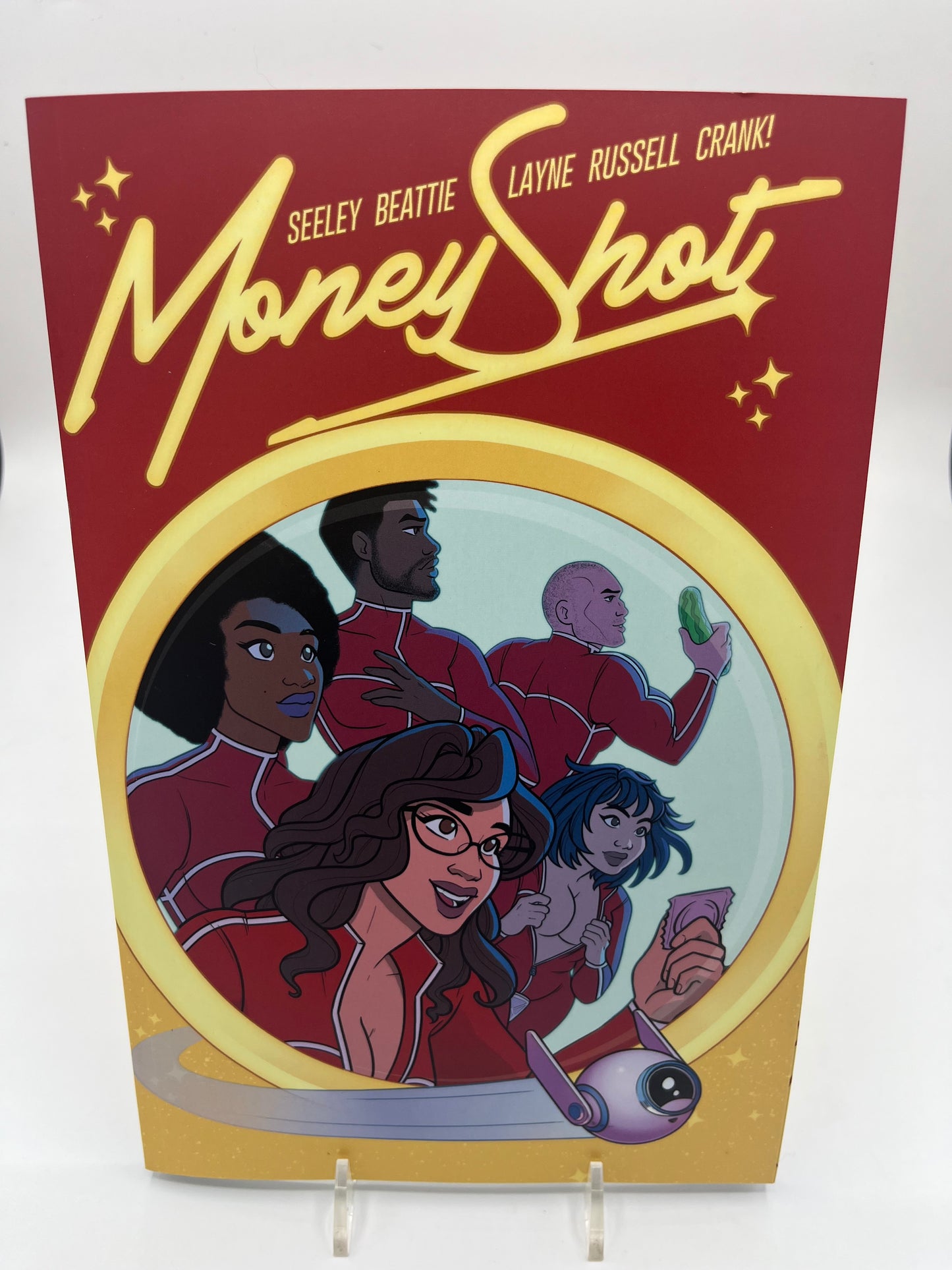 Cover of Money Shot Volume 3 featuring the crew of interplanetary researchers in red uniforms illustrated in a colorful science fiction comic style.