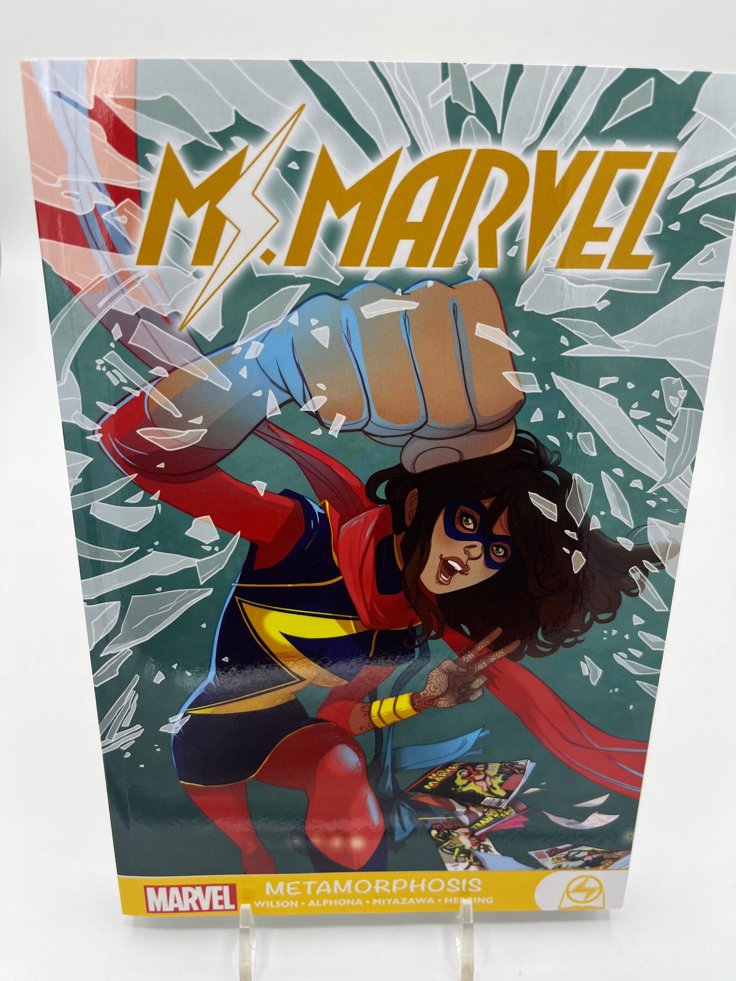 Cover of Ms. Marvel: Metamorphosis featuring Kamala Khan punching through shattered glass while wearing her Ms. Marvel costume.
