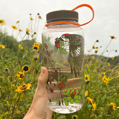Clear chaparral woodpecker water bottle with nature-themed design held in a field of wildflowers