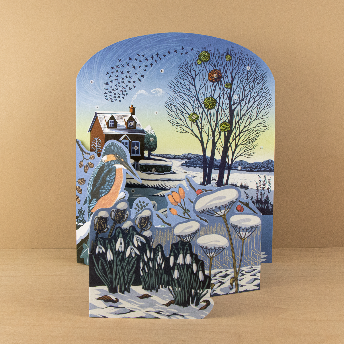 Niki Bowers Winter Riverside Advent Calendar featuring a snowy riverside landscape with a kingfisher, swans, snowdrops, and 24 advent windows.