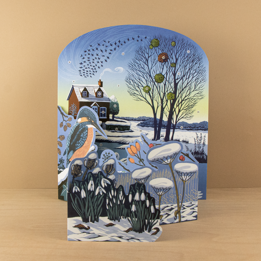 Niki Bowers Winter Riverside Advent Calendar featuring a snowy riverside landscape with a kingfisher, swans, snowdrops, and 24 advent windows.