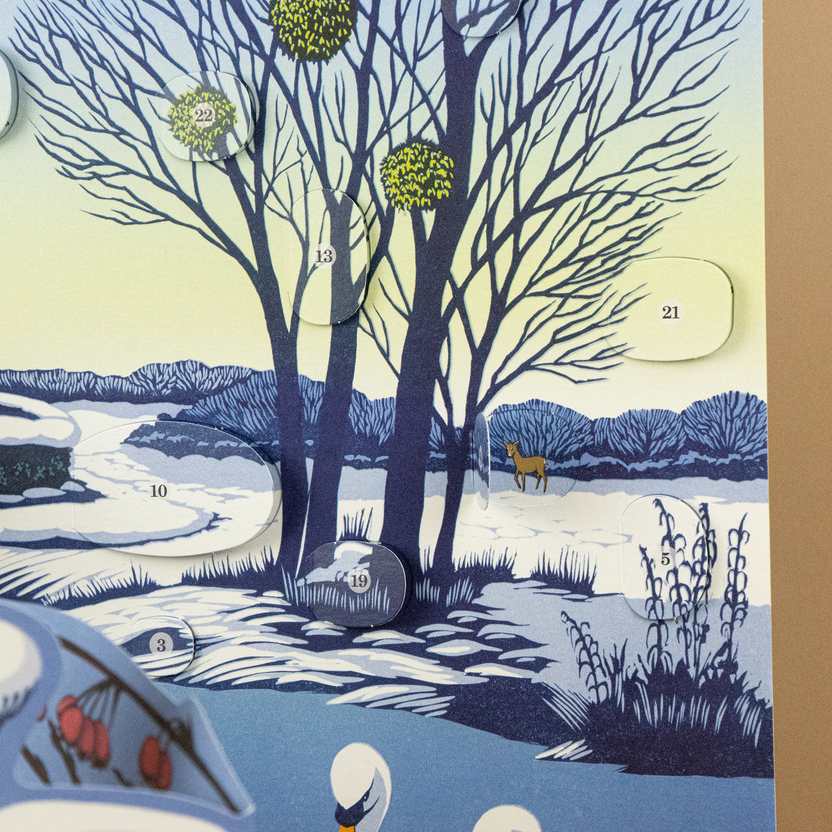 Close-up of the Niki Bowers Winter Riverside Advent Calendar showing numbered advent windows hidden among snowy trees and a winter landscape.