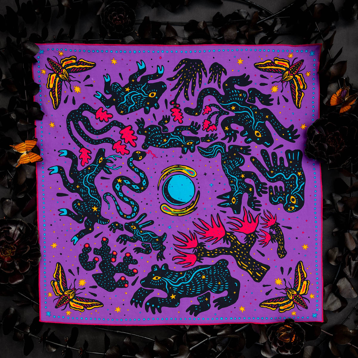 Pine Bones Electric Desert Parade bandana featuring coyotes, ravens, snakes, lizards, desert plants, and a bright blue moon arranged in a vibrant Southwestern-inspired design.