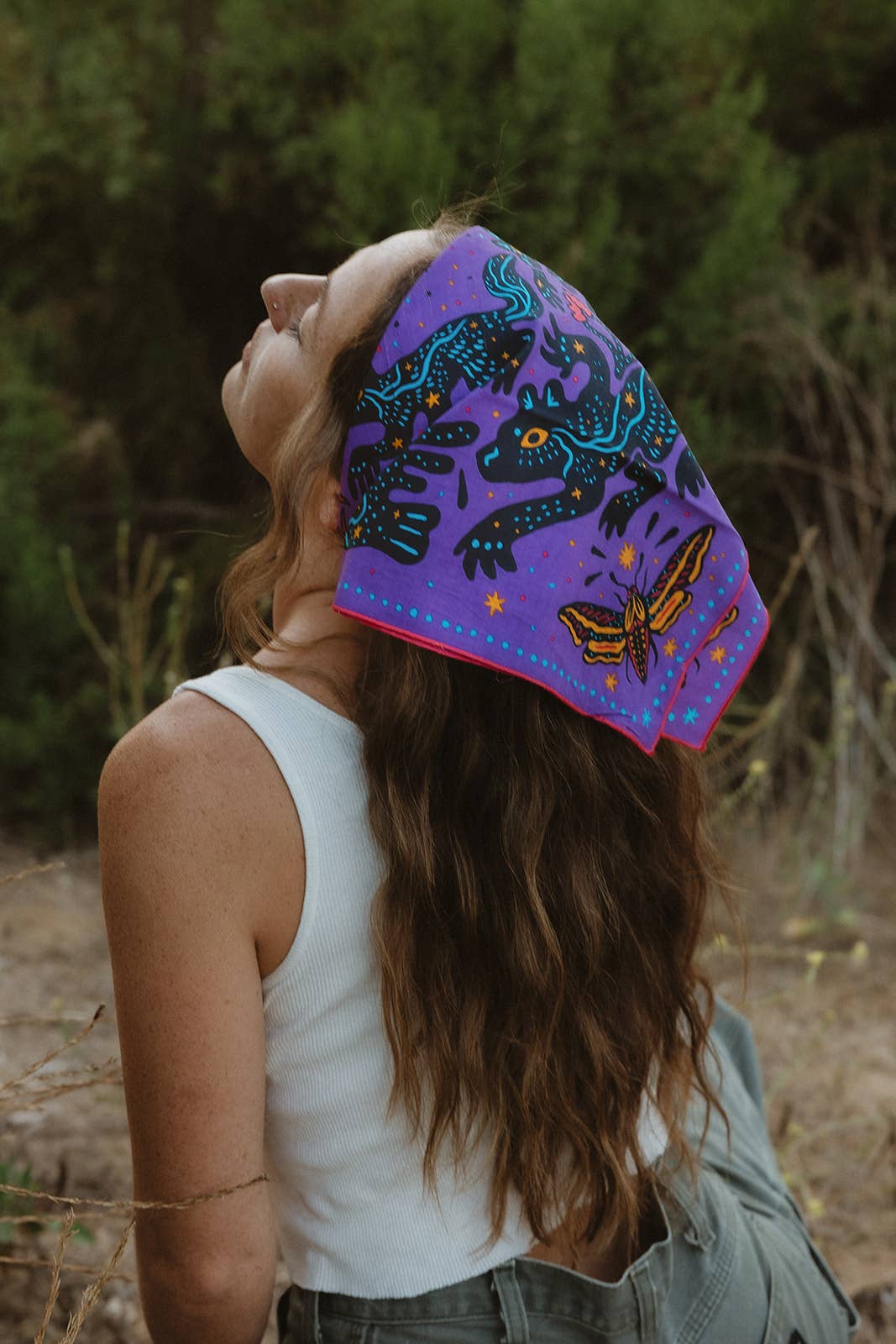 Model wearing the Pine Bones Electric Desert Parade bandana tied as a hair scarf, showcasing the vibrant desert wildlife artwork.