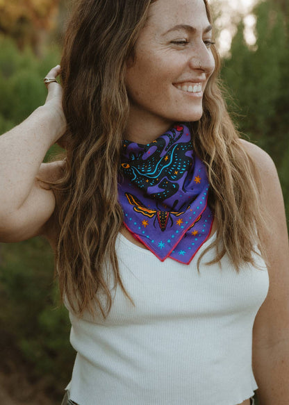 Model wearing the Pine Bones Electric Desert Parade bandana tied as a neck scarf, showcasing the vibrant desert wildlife artwork.