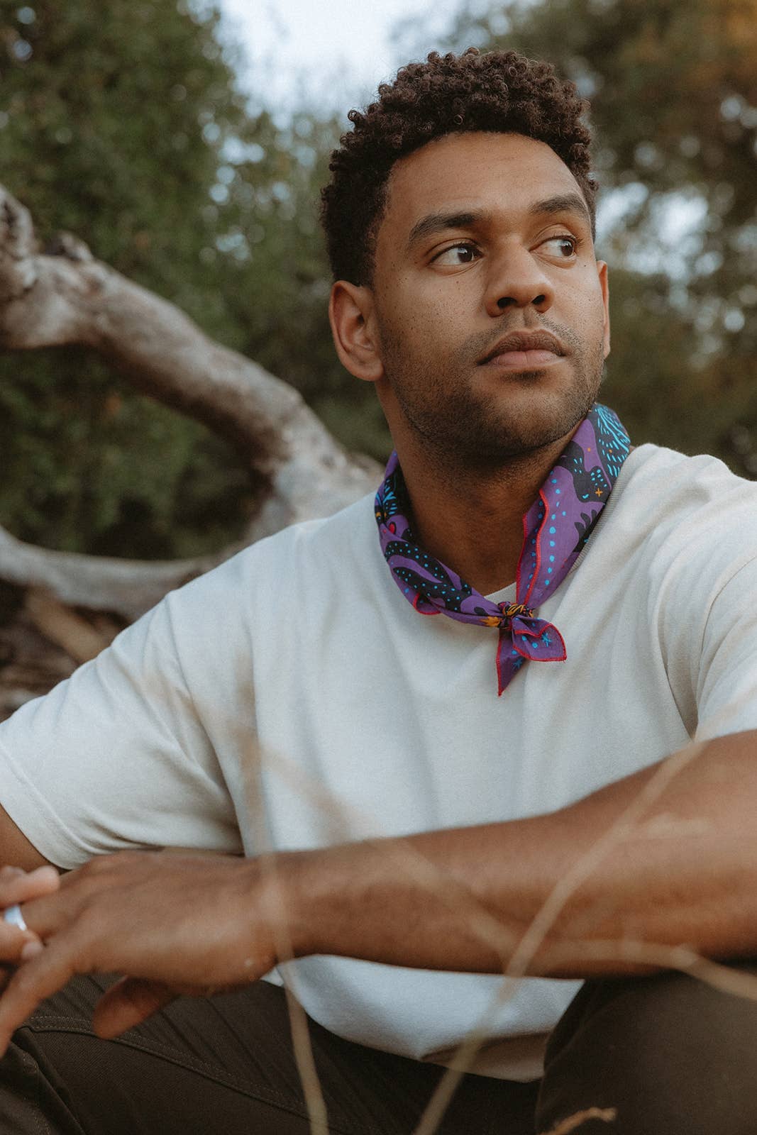 Model wearing the Pine Bones Electric Desert Parade bandana tied as a neckerchief with a white T-shirt in an outdoor setting.