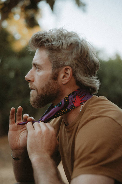 Model tying the Pine Bones Electric Desert Parade bandana around the neck in an outdoor setting.