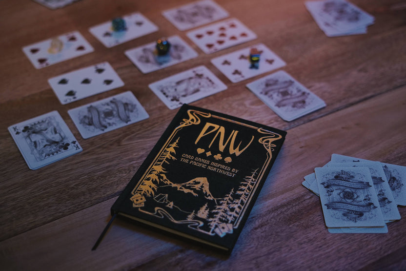 pnw card games book, pacific northwest inspired games, megan wyreweden art, thomas cardwell game designer, nature themed card games, foraging card games, orca salmon mushroom games, coastal forest games, pacific northwest game night, illustrated card game book, camping games with deck of cards, solo and group card games, pnw camping activities, original card games book, pacific northwest gifts, travel