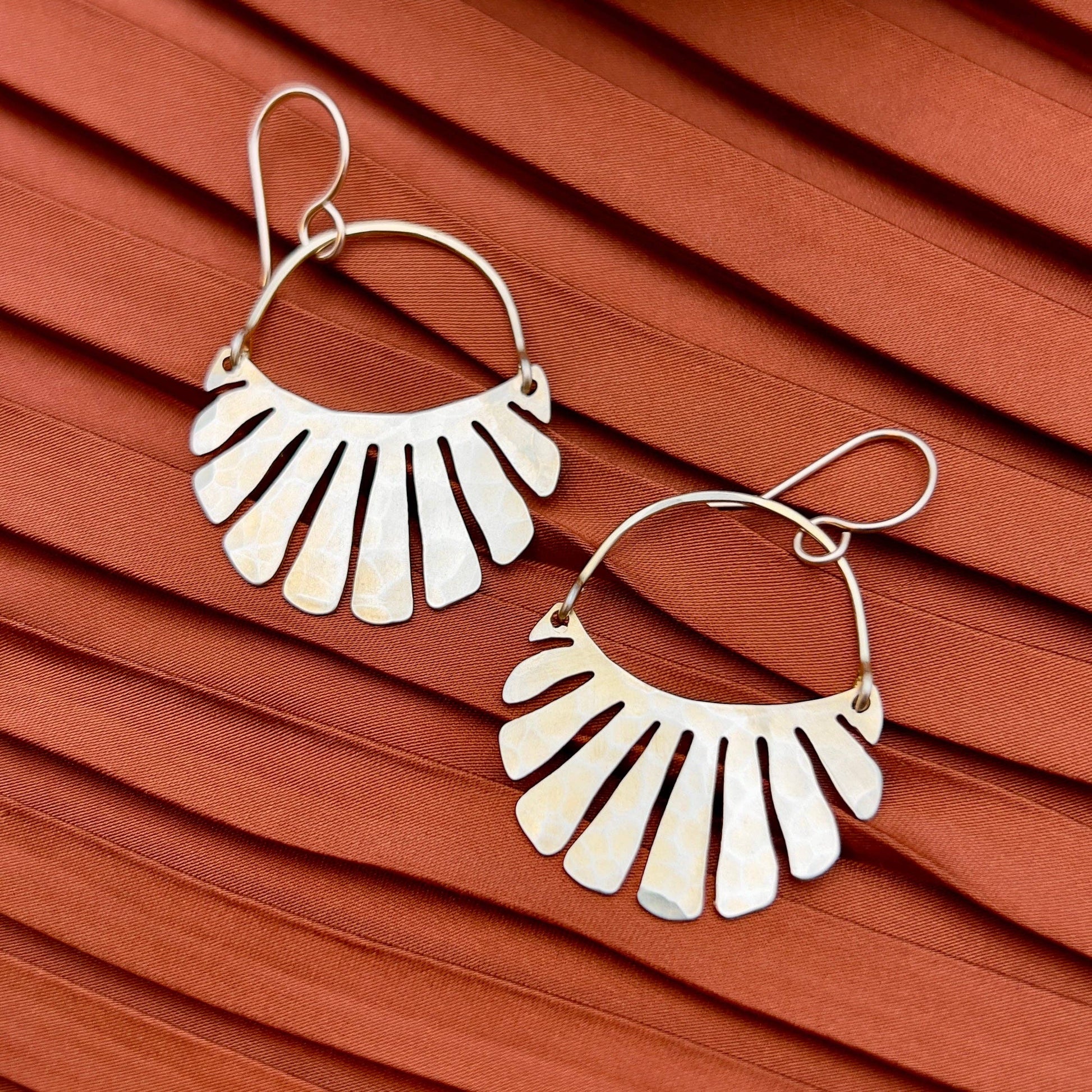 The Freya Earrings by Fluff Hardware are handcrafted gold statement earrings featuring hammered raw brass pendants suspended from hypoallergenic 14k gold filled ear wires. Designed to move beautifully with the wearer, these small-batch earrings offer a warm, luminous finish that works just as well for everyday wear as for special occasions—an artful, versatile gift for lovers of modern, handmade jewelry.