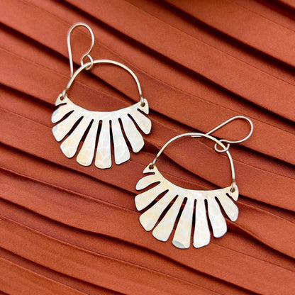 The Freya Earrings by Fluff Hardware are handcrafted gold statement earrings featuring hammered raw brass pendants suspended from hypoallergenic 14k gold filled ear wires. Designed to move beautifully with the wearer, these small-batch earrings offer a warm, luminous finish that works just as well for everyday wear as for special occasions—an artful, versatile gift for lovers of modern, handmade jewelry.