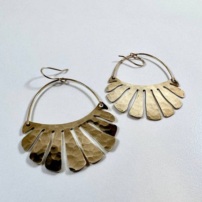 The Freya Earrings by Fluff Hardware are handcrafted gold statement earrings featuring hammered raw brass pendants suspended from hypoallergenic 14k gold filled ear wires. Designed to move beautifully with the wearer, these small-batch earrings offer a warm, luminous finish that works just as well for everyday wear as for special occasions—an artful, versatile gift for lovers of modern, handmade jewelry.