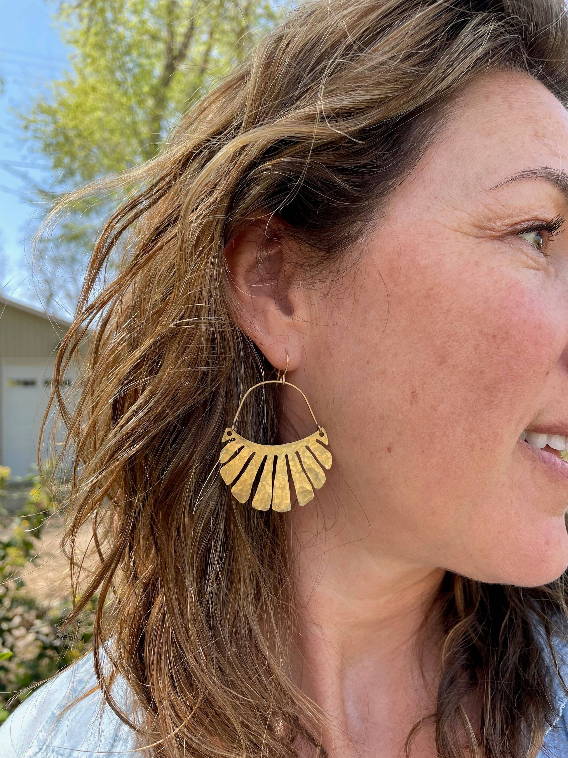 The Freya Earrings by Fluff Hardware are handcrafted gold statement earrings featuring hammered raw brass pendants suspended from hypoallergenic 14k gold filled ear wires. Designed to move beautifully with the wearer, these small-batch earrings offer a warm, luminous finish that works just as well for everyday wear as for special occasions—an artful, versatile gift for lovers of modern, handmade jewelry.