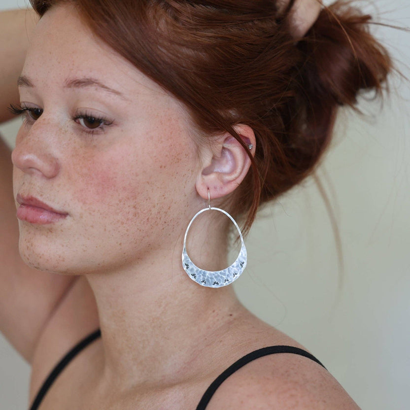 Fluff Hardware Lumos Earrings are handcrafted statement hoops with an organic shape and a one-of-a-kind stamped, textured finish. Designed to feel subtle yet striking, these small-batch earrings dangle from hypoallergenic sterling silver ear wires and add luminous movement to any outfit. A beautiful gift and an easy everyday accessory for anyone who loves modern, nature-inspired jewelry with artisan detail.