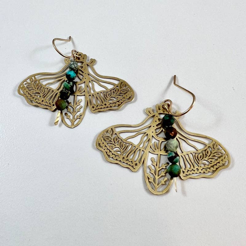 The Peppered Moth Earrings (Large) by Fluff Hardware are handcrafted gold statement earrings featuring a raw brass moth pendant accented with turquoise beads. Finished with hypoallergenic 14k gold filled ear wires, these nature-inspired earrings bring color, movement, and meaning to everyday wear. A beautiful small-batch piece and a thoughtful gift for anyone drawn to symbolic jewelry and artisan craftsmanship.